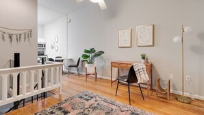 Una sala de estar moderna con un ventilador de techo, un comedor con mesa y sillas, una planta pequeña y obras de arte en la pared.