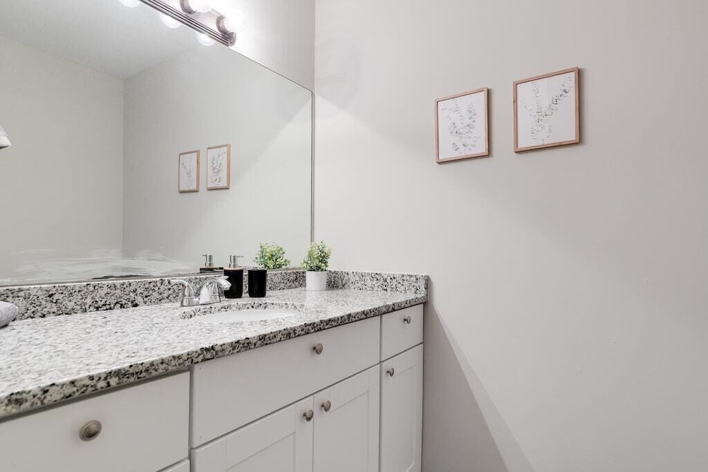 A bathroom with a granite countertop, a sink, a mirror, and framed artwork on the wall.