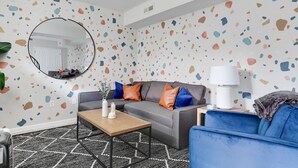 Una sala de estar moderna con un sofá gris, un sillón azul y un espejo redondo en la pared.