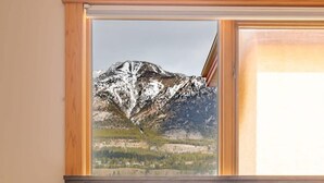 Quarto com cama, mesa de cabeceira, luminária e janela com vista para as montanhas.