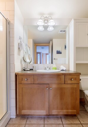 A bathroom with a wooden vanity, a round mirror, a sink, and a shower area.