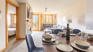 Uma sala de jantar com mesa posta para quatro pessoas, lareira e sofá ao fundo.