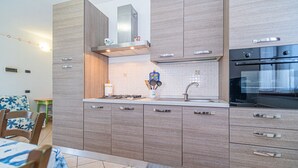 A modern kitchen with wooden cabinets, a stainless steel range hood, a built-in oven, and a tiled backsplash. - Appartamento Villa da 2 Fino a 4 Persone Giardino (Capoliveri)