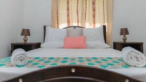 Een net opgemaakt bed met een beddekleed met dessin, kussens en opgerolde handdoeken.