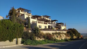 A multi-story residential building with balconies, situated on a hillside with a clear sky. - 22C Christina Hilltop Apartment panoramic views. (Peyia)