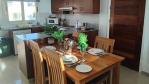 A kitchen with wooden cabinets, a microwave, and a dining table set for four. - 22C Christina Hilltop Apartment panoramic views. (Peyia)