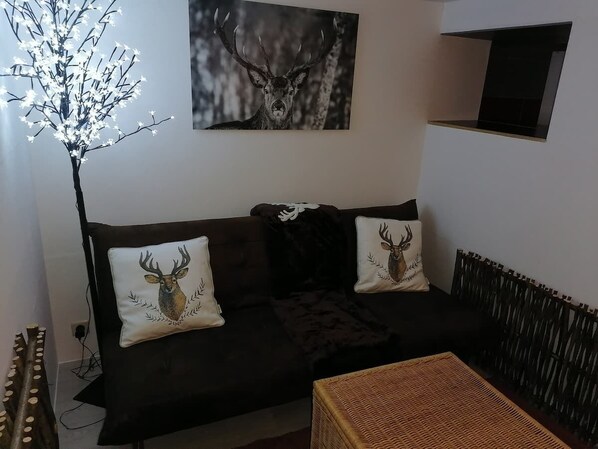 A living room with a dark brown sofa, two decorative pillows with deer images, a black throw blanket, a woven coffee table, a floor lamp with branches, and a framed deer painting on the wall. - Studio Galaxy in the center of Libramont (Libramont-Chevigny)