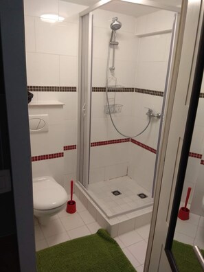 A shower with a glass door, a white toilet, and a red toilet brush. - Studio Galaxy in the center of Libramont (Libramont-Chevigny)