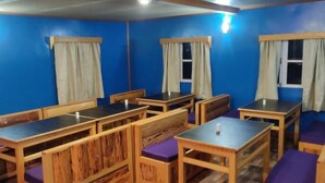 Una habitación con mesas y bancos de madera, paredes azules y ventanas con cortinas.