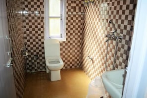 A bathroom with checkered tile walls, a toilet, a shower, and a window. - Rufina Lachung De'Crown (Chungthang)
