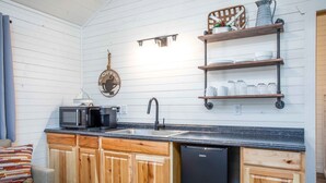 A compact kitchen with wooden cabinets, a black dishwasher, a microwave, and a coffee-themed wall decoration.