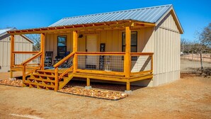 A small wooden cabin with a porch, a staircase, and a fenced area with a bird feeder.