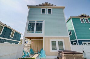 A two-story house with a covered porch, a hot tub, and a small deck with chairs. - Warm Waters Oasis at Devonshire Place (Kill Devil Hills)