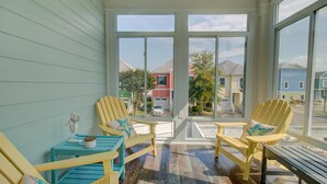 A sunroom with large windows, wooden chairs, a small table, and a bench. - Warm Waters Oasis at Devonshire Place (Kill Devil Hills)