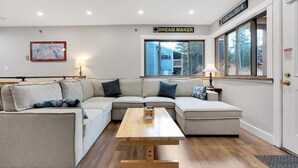 A modern living room with a sectional sofa, a wooden coffee table, and a large window with a view of a house.