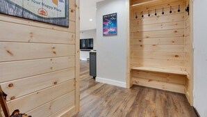 A wooden interior with a wall-mounted coat rack, a poster, and a glimpse of a kitchen area.