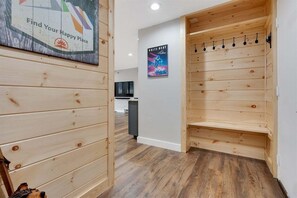 Un interior de madera con un perchero en la pared, un cartel y una vista parcial de una cocina.
