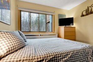 A bedroom with a bed, a dresser, a television, and a window with a view of trees.