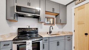 A kitchen with grey cabinets, a stainless steel stove, a microwave, and a sink.