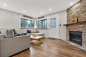 A living room with a stone fireplace, a sofa, a coffee table, and a door labeled 'DREAM MAKER.'