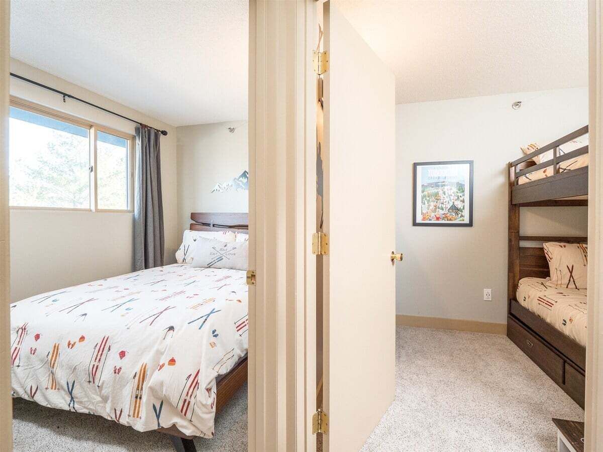 A bedroom with a bed, a bunk bed, a window, and a framed picture on the wall.