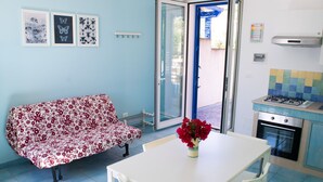 A kitchen with a gas stove, a dining table with chairs, a sofa, and a vase of flowers.