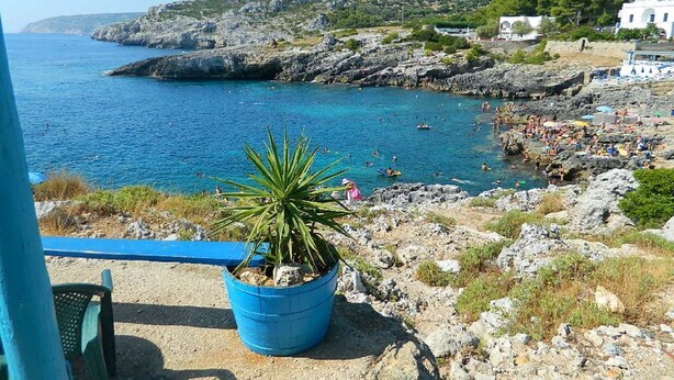 A coastal view with a rocky beach, a clear blue sea, and a few boats.