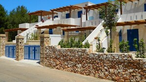 A row of white buildings with blue shutters, stone walls, and wooden pergolas.