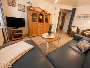 A living room with a sofa, a television, a wooden cabinet, and a small table with a plant.