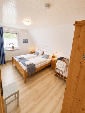 A bedroom with a wooden bed, bedside tables, a crib, a window with curtains, and a ceiling light.