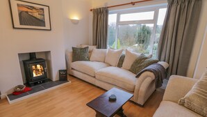 A cozy living room with a fireplace, a sofa, a coffee table, and a window with curtains. - Sea Change (Whitby)