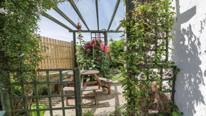 A garden with a wooden pergola, a wooden table, and chairs. There is a wooden fence and a white wall in the background. - Sea Change (Whitby)