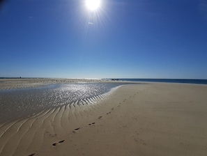 Ranta, jossa hiekassa näkyy jalanjälkiä ja aaltojen aiheuttamia kuvioita, kirkas taivas ja aurinko paistaa.