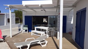 Un espace extérieur abrité, avec une table et des chaises, un fauteuil de relaxation et une porte bleue.