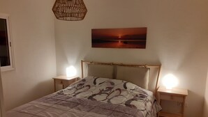 Une chambre à coucher comprenant un lit, deux tables de chevet, une petite table, une lampe suspendue et un tableau accroché au mur.