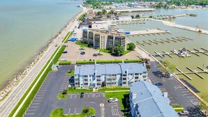 An aerial view of a waterfront property with a parking lot, a building with a flat roof, and a marina with boats.