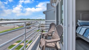 A balcony with two Adirondack chairs, a view of a marina, and a bed with a striped bedspread.