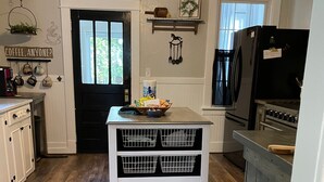 A kitchen with a black refrigerator, a white table with baskets, wooden flooring, and a black door.