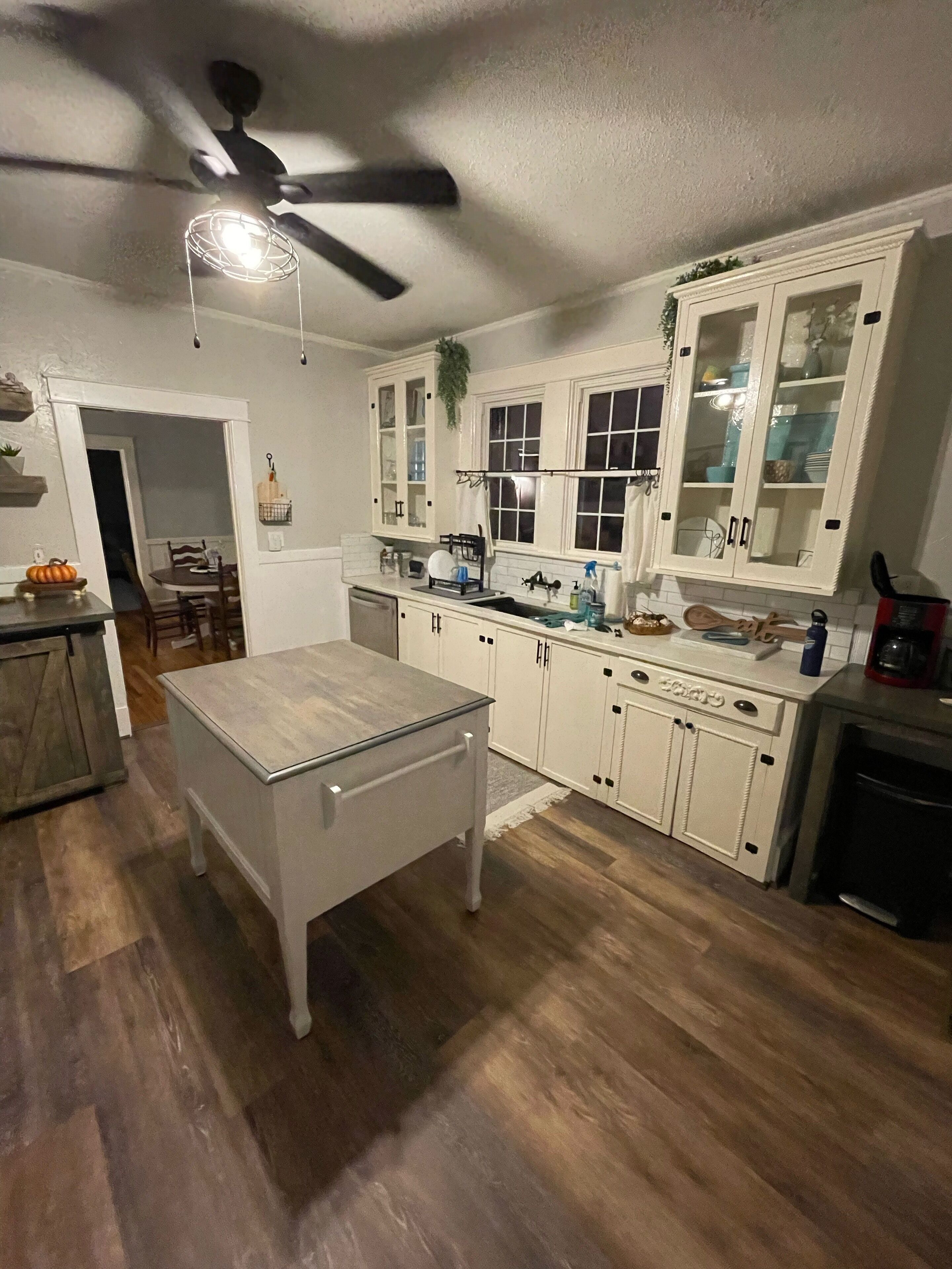 A kitchen with white cabinets, a wooden table, and a ceiling fan.