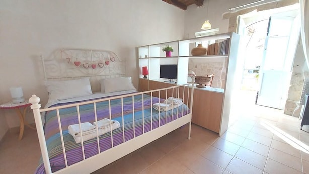 A bedroom with a bed, bedside table, and a small desk area with shelves.