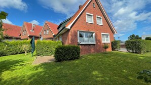 A red-brick house with a sloped roof, white windows, and a well-maintained lawn. - Strandläufer (Wangerland)