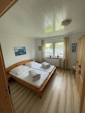 Une pièce avec deux lits en bois, une fenêtre avec des rideaux, un radiateur et une armoire en bois.