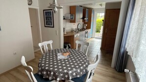 A dining area with a round table covered in a star-patterned tablecloth, surrounded by white chairs. - Strandläufer (Wangerland)