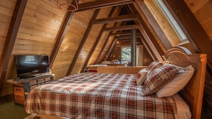 Een gezellig slaapkamer onder de pannen met houten balken, een bed met geruite beddengoed, een televisie op een houten dressoir, en een raam dat natuurlijk licht binnenlaat.