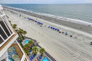 A beach view from a hotel balcony with a pool area and palm trees.