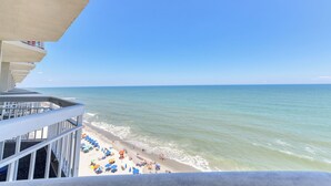A balcony with a view of a beach, including umbrellas and people.