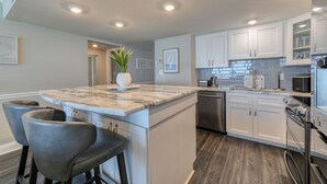 A modern kitchen with white cabinets, a marble island, and stainless steel appliances.