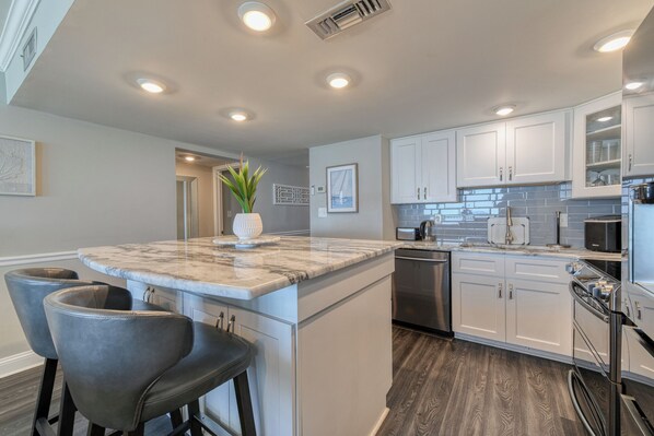 A modern kitchen with white cabinets, a marble island, and stainless steel appliances.