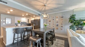 A modern kitchen with a central island, bar stools, and a dining table.