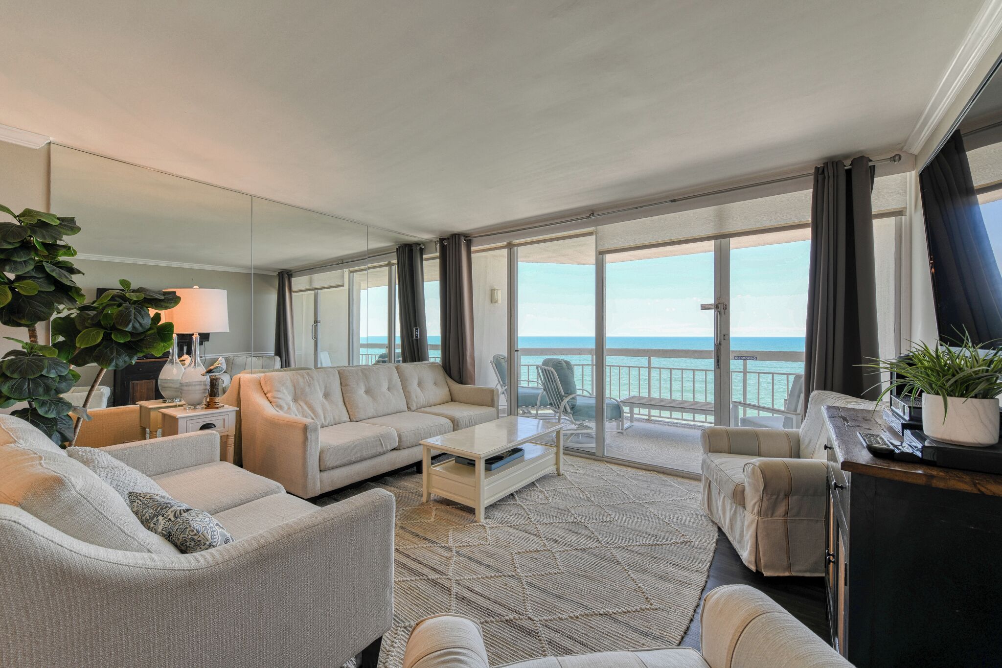A spacious living room with a large sofa, a coffee table, and a view of the ocean through large sliding glass doors.